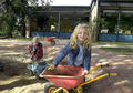Ein Mädchen mit einer Schubkarre im Sandkasten. Im Hintergrund ein Junge mit einem kleinen Baufahrzeug