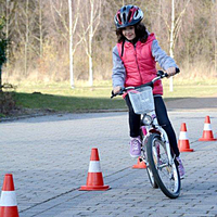 Ein Mädchen einem Fahrrad fährt im Slalom an diversen rot-weißen Hütchen vorbei