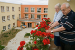Eine Bewohner und eine Bewohnerin stehen auf einem Balkon, welcher mit Blumen bepflanzt ist