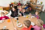 Kinder und eine Erzieherin sitzen an einem Tisch beim Essen