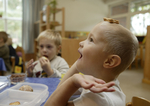 Ein Junge spielt mit einem Keks, ein anderer Junge im Hintergrund isst