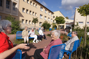 Eine Gruppe von Bewohnerinnen und Bewohnern sitzt auf Bänken vor dem Gebäude des Wohn- und Pflegeheims Am Eikel.